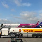 Avião comercial sendo abastecido por um caminhão-tanque da Shell no pátio de um aeroporto.