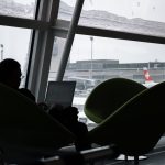 Pessoa usando um laptop no saguão de um aeroporto, com aviões visíveis ao fundo.