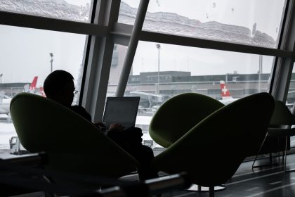 Pessoa usando um laptop no saguão de um aeroporto, com aviões visíveis ao fundo.