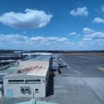 Vista aérea de um aeroporto ensolarado, com pista de pouso e edifícios do terminal.