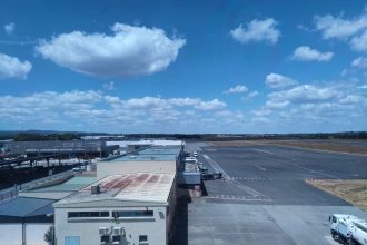 Vista aérea de um aeroporto ensolarado, com pista de pouso e edifícios do terminal.