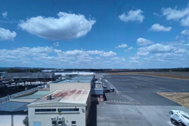 Vista aérea de um aeroporto ensolarado, com pista de pouso e edifícios do terminal.