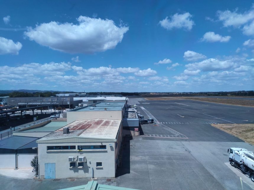 Vista aérea de um aeroporto ensolarado, com pista de pouso e edifícios do terminal.